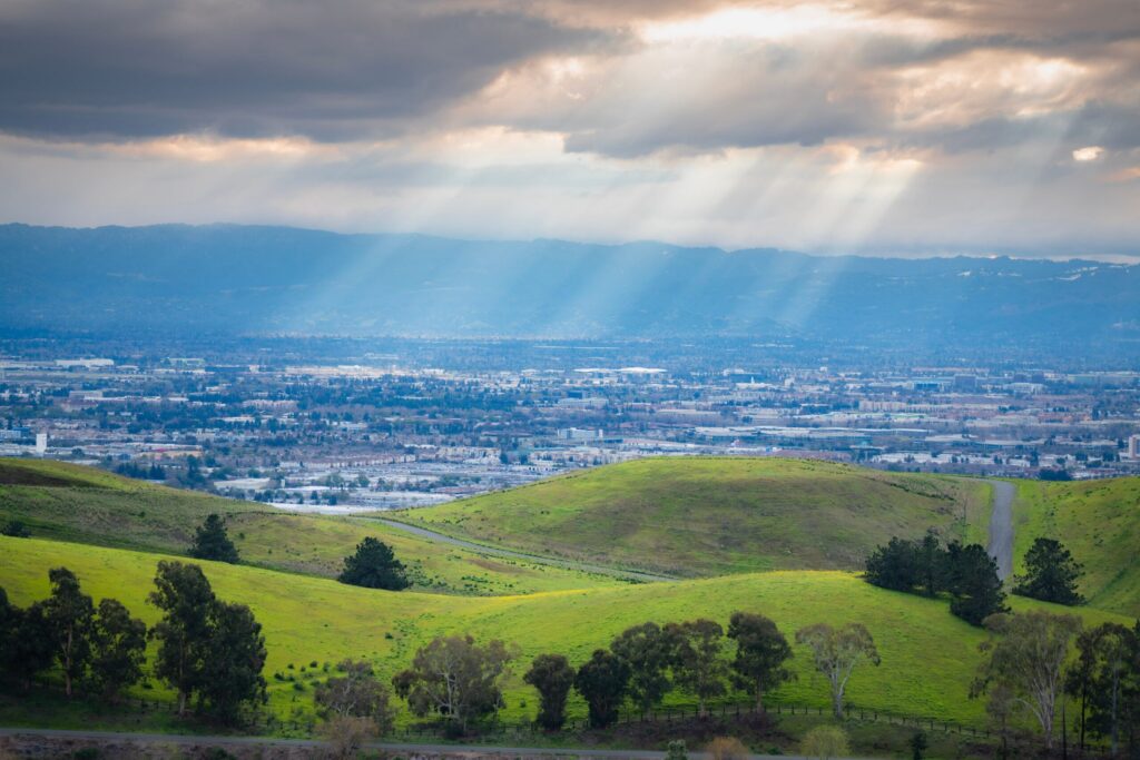 Breathtaking view of green hills with sun rays over a town in the valley.